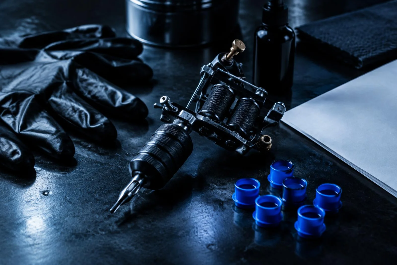 Coil tattoo machine, gloves and blue ink caps on a studio table